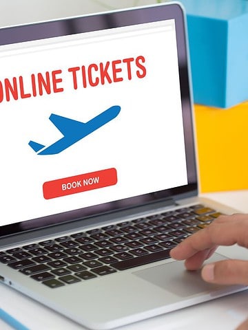 Laptop screen displaying "Online Tickets" with an airplane graphic and a "Book Now" button; person typing.