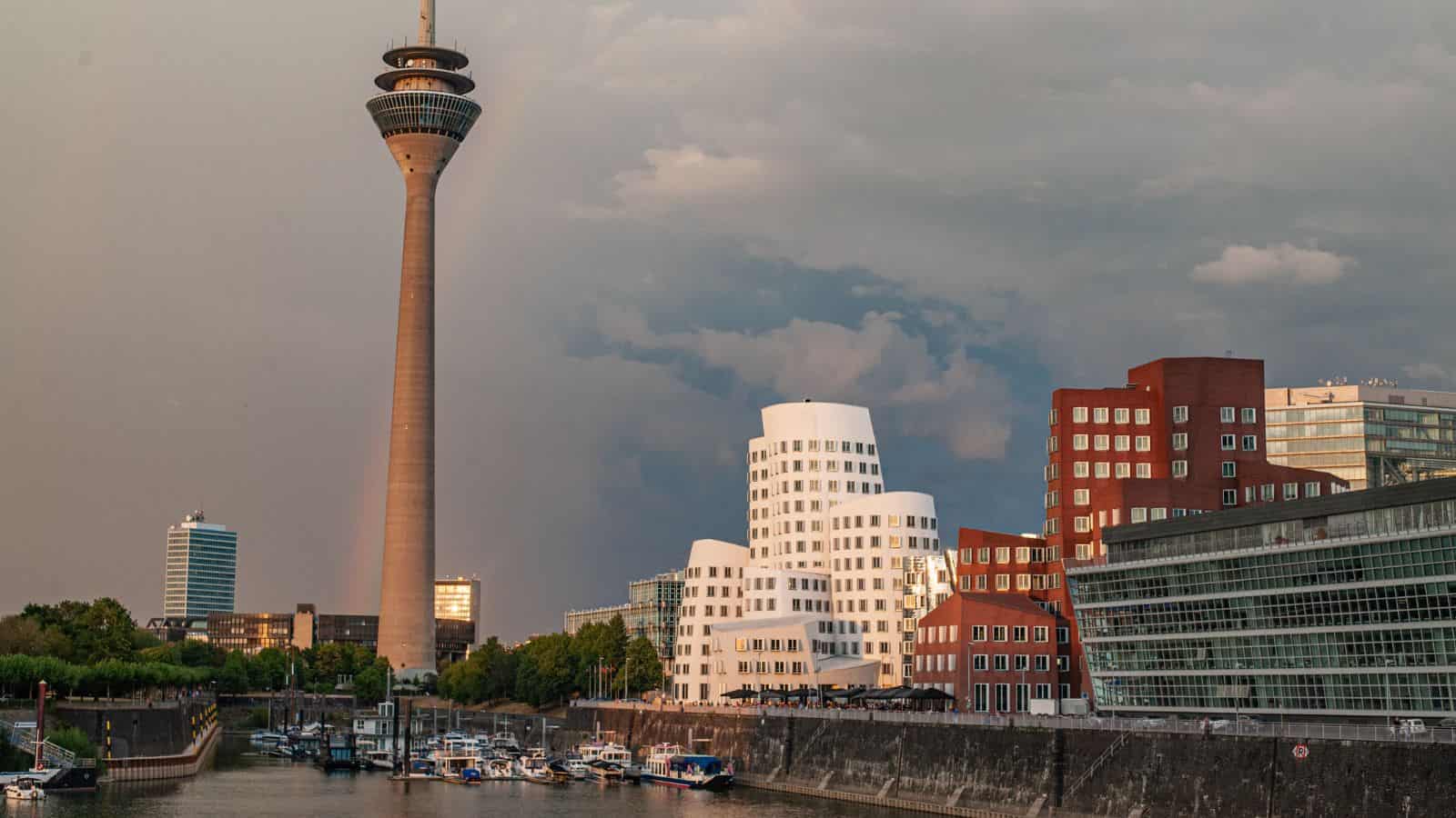 Modern buildings and a tall tower by a waterfront marina under a cloudy sky in D&uuml;sseldorf, Germany.
