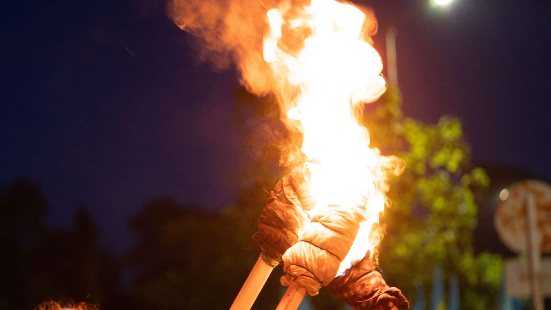 Three gloved hands holding burning torches together at night, flames bright against a dark background.