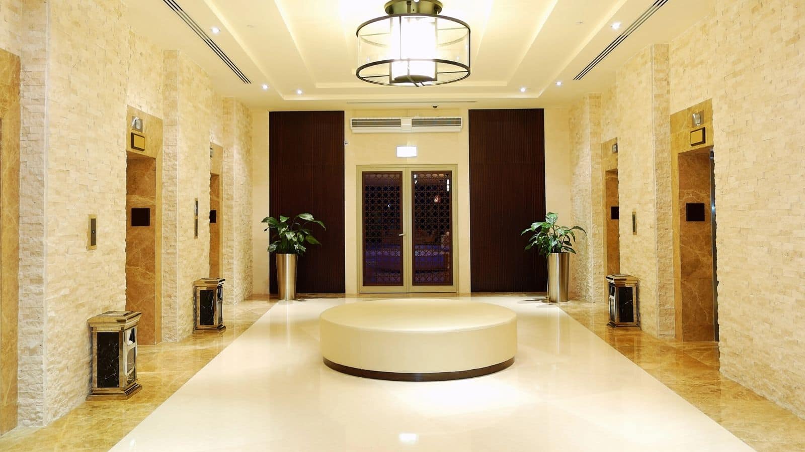 Luxurious hotel elevator lobby with marble floors, beige walls, plants, and a round cream-colored bench&mdash;perfect for travelers over 35 looking for refined comfort.