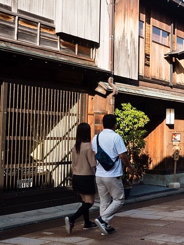 People walk along a street with traditional wooden buildings on a sunny day.