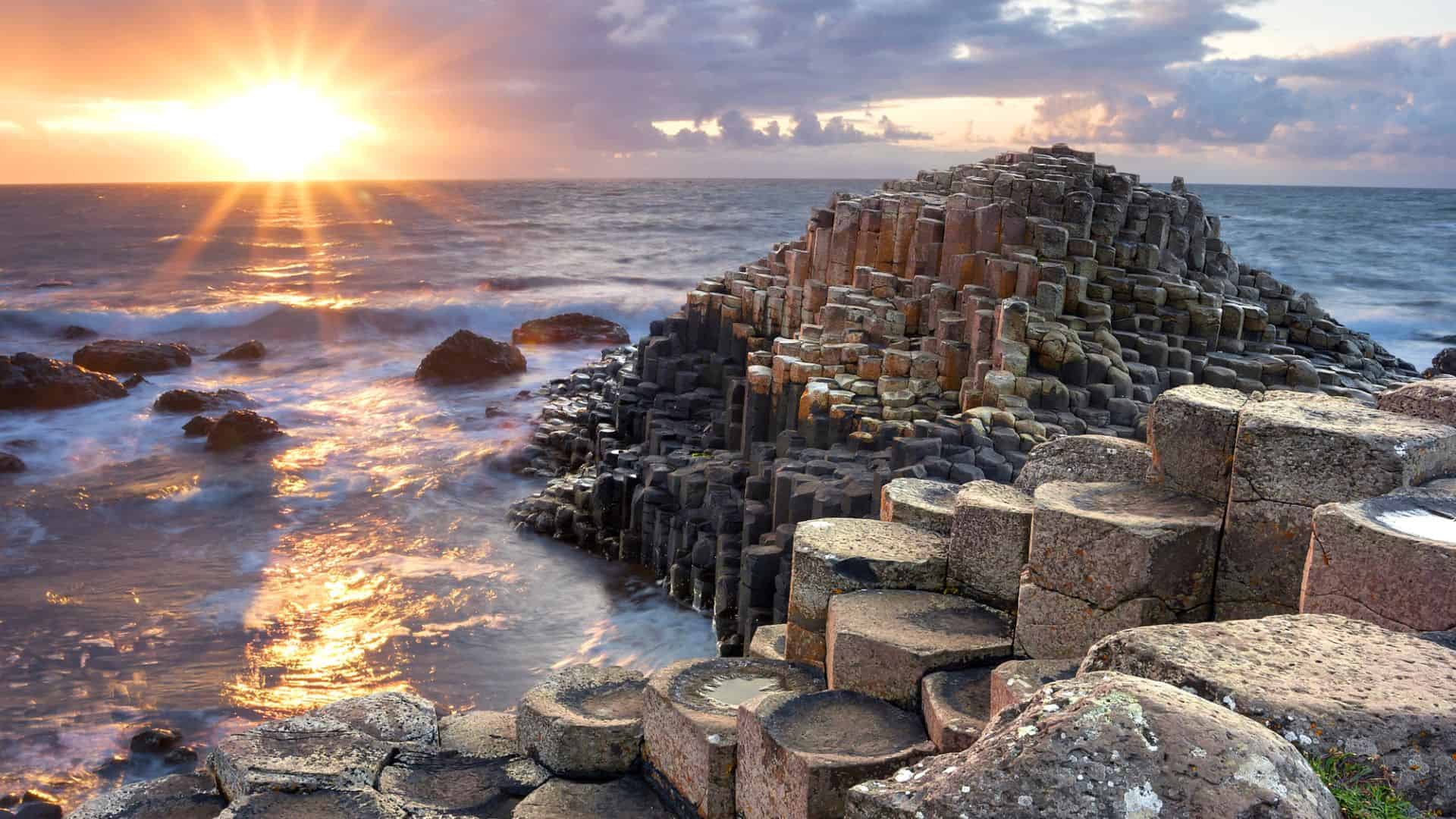 Sunset over the Giant’s Causeway with hexagonal basalt columns by the ocean.
