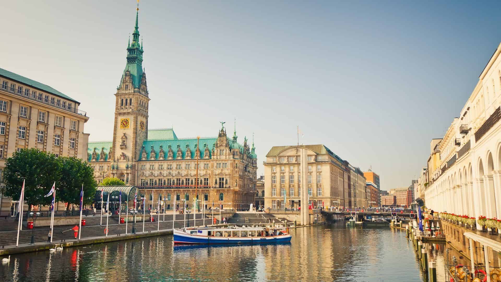 Boat on a canal in front of Hamburg’s historic Rathaus city hall under a clear blue sky.