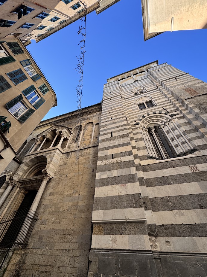 Stone church tower with striped facade in Genoa, Italy, surrounded by tall buildings under a clear blue sky—an iconic sight to discover in just 24 hours.