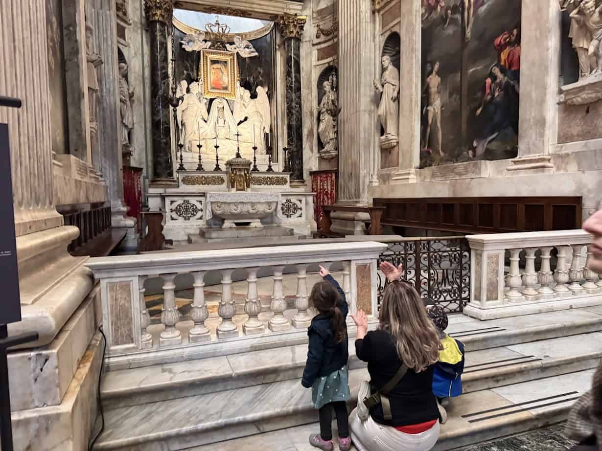 Three children and an adult admire an ornate marble altar inside a grand, historic cathedral in Genoa, Italy.