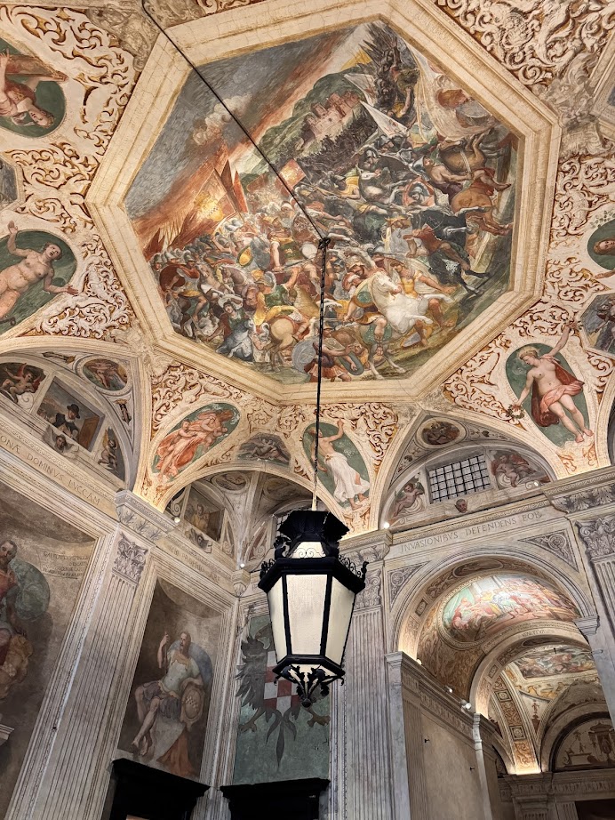 Ornate ceiling frescoes and a large hanging lantern adorn this grand hall in Genoa, Italy, where arches and detailed wall art can be admired 24 hours a day.