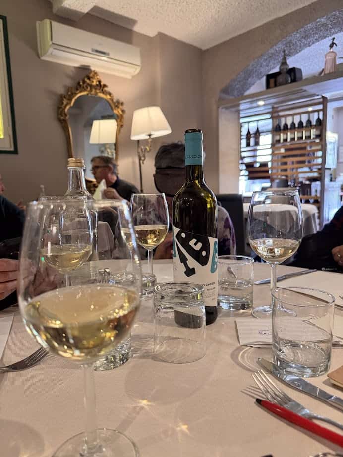 Table set with wine glasses, a wine bottle, water glasses, and diners enjoying a cozy restaurant—perfect for experiencing authentic flavors during 24 hours in Genoa.