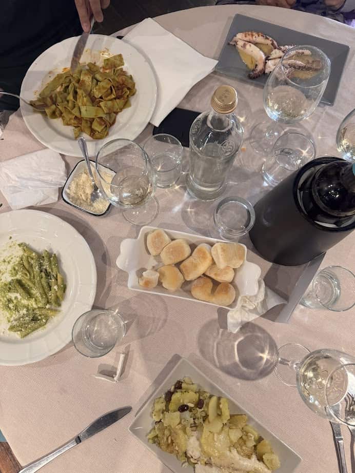 Overhead view of a table set with pasta dishes, bread rolls, drinks, and various glassware—capturing the flavors of Genoa, perfect for anyone dreaming of 24 hours in Genoa or savoring the authentic tastes of Italy.