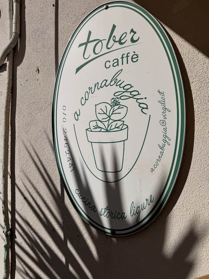 Oval sign for "Tober caffè" with a potted plant illustration, on a sunlit wall with leaf shadows—perfect for a cozy stop during your 24 hours in Genoa, Italy.