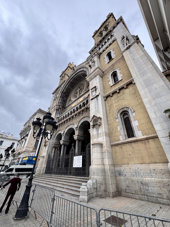 A large stone cathedral with arched entrances and ornate details rises beneath a cloudy sky—a highlight for any Tunisia itinerary 1 day.