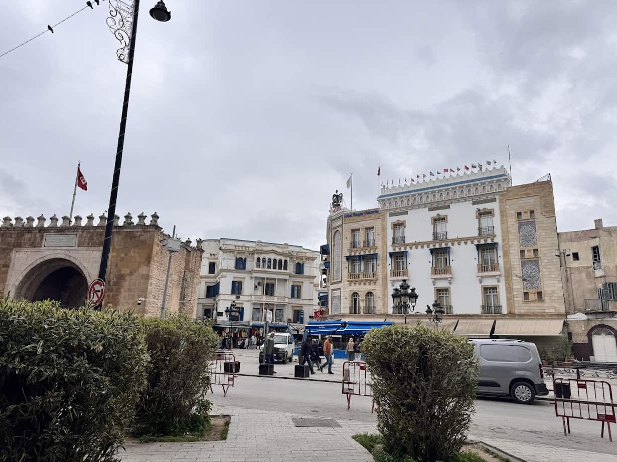 A city street with historic buildings, a stone gate, parked cars, and cloudy skies overhead—perfect for a Tunisia itinerary 1 day adventure.