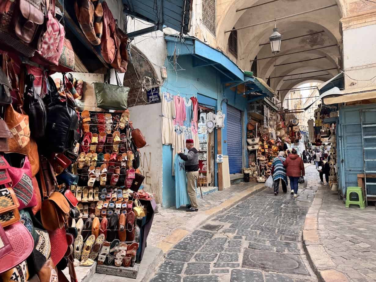 Narrow cobblestone street lined with colorful shops and people walking through a bustling market—a perfect highlight for your Tunisia itinerary 1 day adventure.