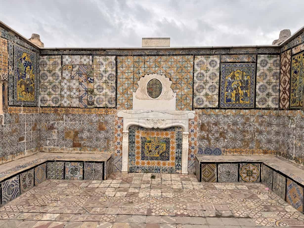 Colorful ornate tiled courtyard wall with a white stone fireplace and patterned tile floor evokes the charm you'd find on a Tunisia itinerary 1 day, all set beneath a cloudy sky.