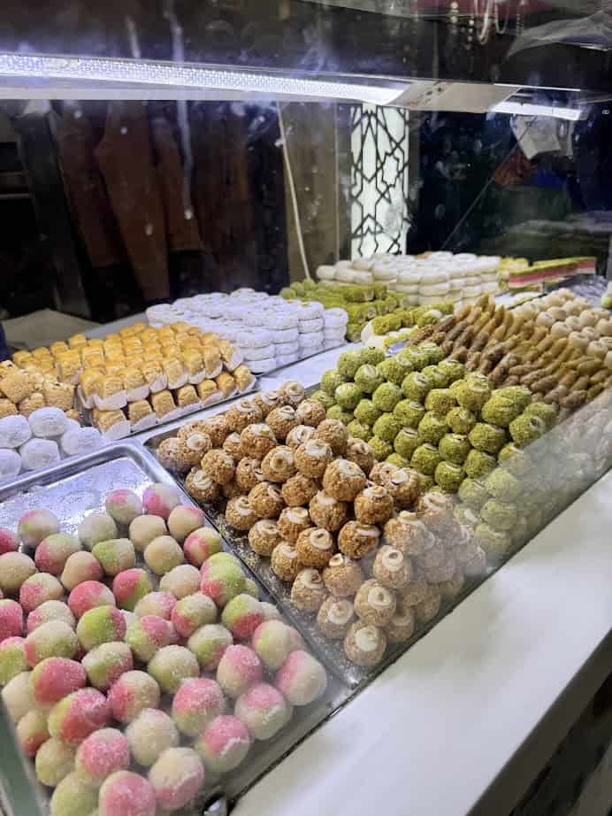 Assorted colorful sweets and pastries displayed in rows behind a glass counter at a bakery or market, perfect for a quick stop on your Tunisia itinerary 1 day adventure.