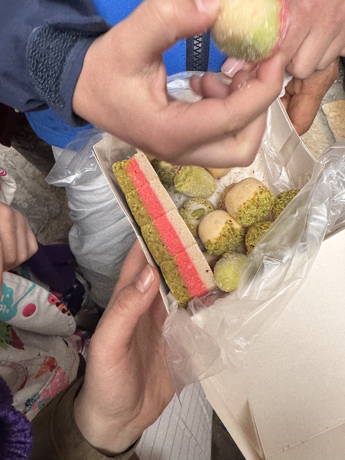 A hand holds a box of assorted colorful sweets while others reach in to take some, sharing treats that could be a delightful stop on your Tunisia itinerary 1 day adventure.