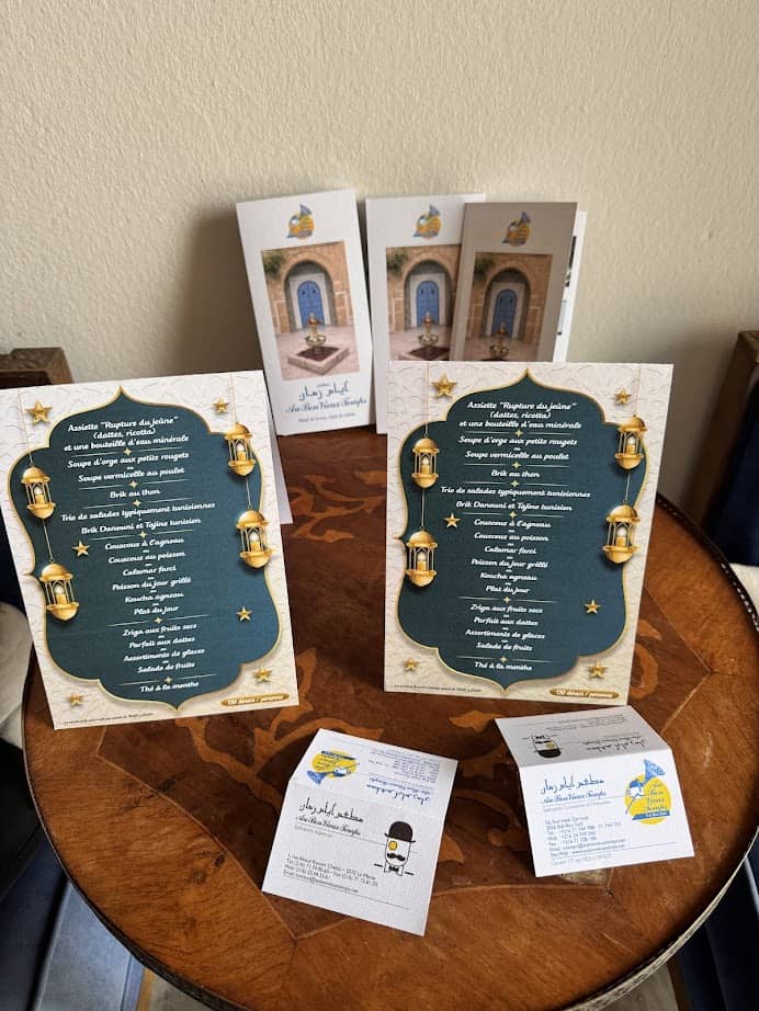 Two standing decorative menus and cards displayed on a wooden table, with brochures—including a tunisia itinerary 1 day guide—propped up behind them.