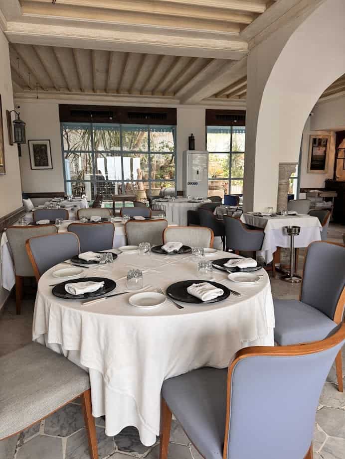A round dining table set with white cloth and plates in a bright, elegant restaurant with a wooden ceiling—an ideal spot to savor local flavors on your Tunisia itinerary 1 day adventure.