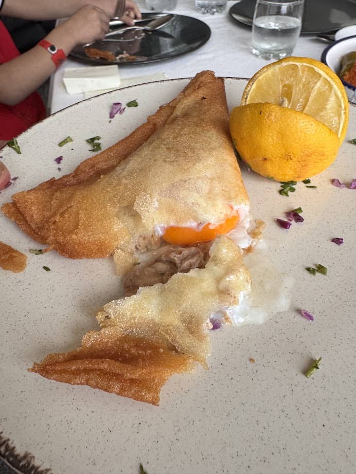A crispy crepe with a runny egg yolk, garnished with half a lemon, on a beige plate—perfect for starting your Tunisia itinerary 1 day adventure.