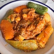 A bowl of couscous topped with vegetables, chickpeas, and meat in a tomato-based sauce—an essential dish to try on your Tunisia itinerary 1 day adventure.