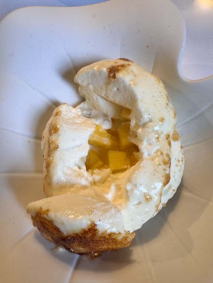 A dessert with fluffy meringue, creamy sauce, and diced yellow fruit on a white plate&mdash;a sweet treat to enjoy after exploring your Barcelona itinerary or during 4 days in Barcelona.