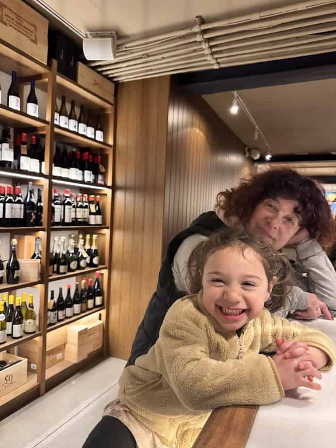 Smiling child and woman at a counter with shelves of wine bottles in the background&mdash;capturing a perfect moment from a family-friendly Barcelona itinerary.