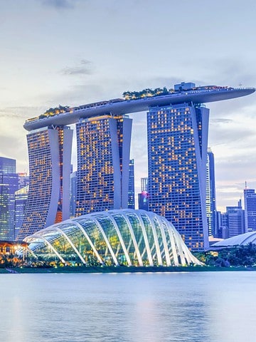 Singapore skyline at dusk featuring Marina Bay Sands and Gardens by the Bay domes, reflected in the water.