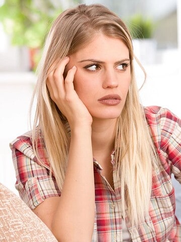 A woman looks frustrated while a man sits in the background with his face in his hands.