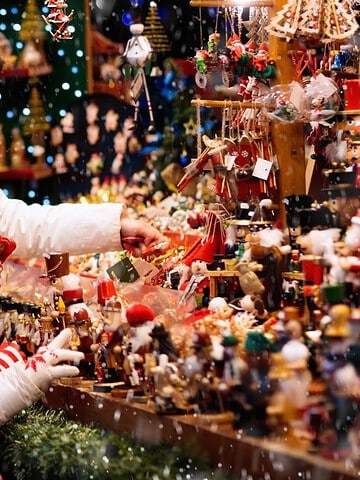 A woman and two children in winter clothes look at toys at a festive outdoor market in the snow.
