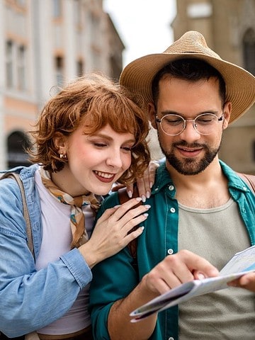 A smiling couple stands outdoors, reading a map together in a city with historic buildings.