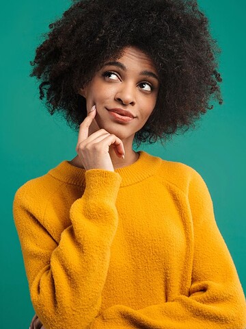Woman in yellow sweater with hand on chin, looking thoughtful against a plain teal background.