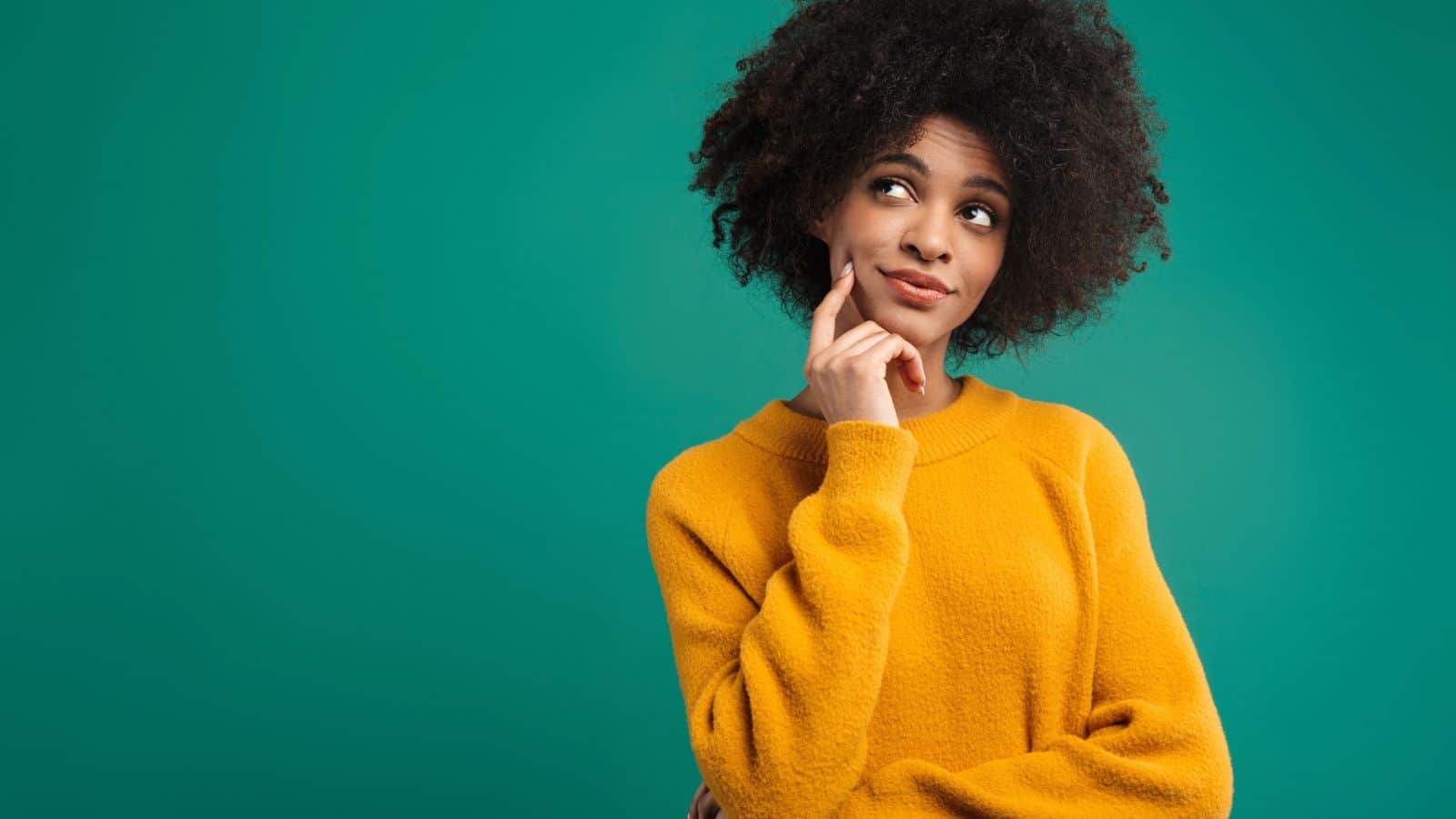 Woman in yellow sweater with hand on chin, looking thoughtful against a plain teal background.