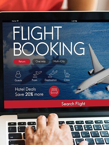 Person booking a flight online on a laptop, holding a credit card, with a phone and a map nearby.