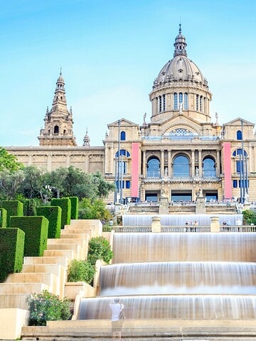 Grand palace with domes and towers, cascading fountains, and manicured gardens under a blue sky.