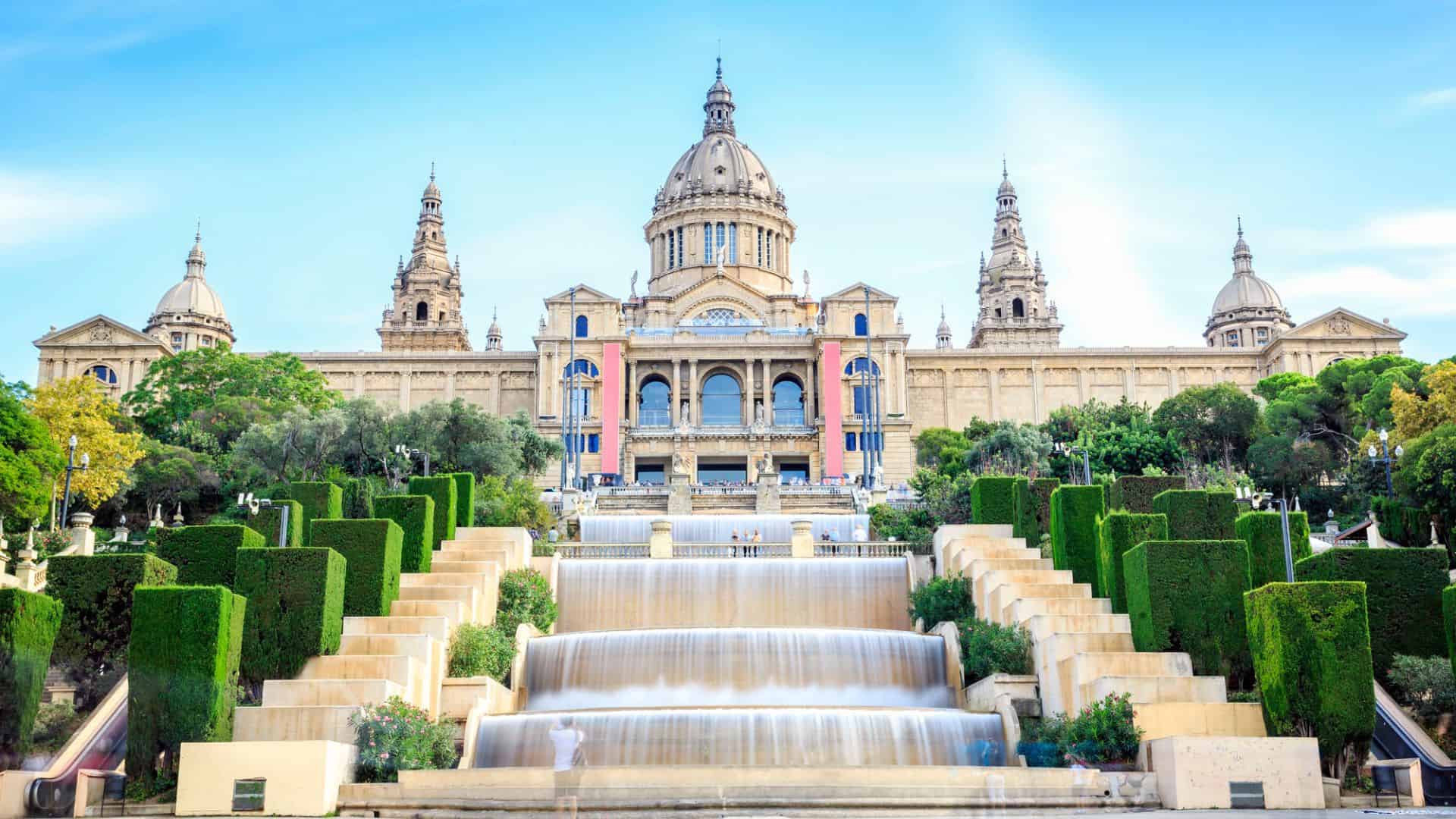 Grand palace with domes and towers, cascading fountains, and manicured gardens under a blue sky.