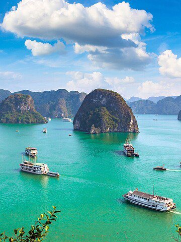 Tour boats sail on turquoise water among limestone islands under a blue sky with clouds.