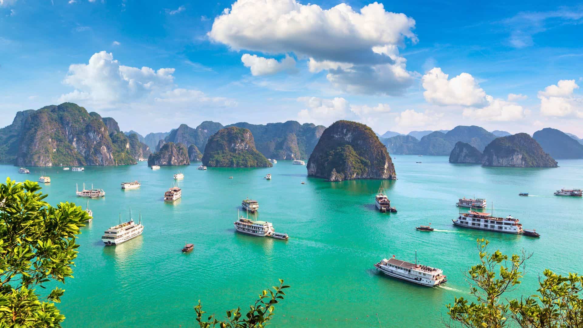 Tour boats sail on turquoise water among limestone islands under a blue sky with clouds.