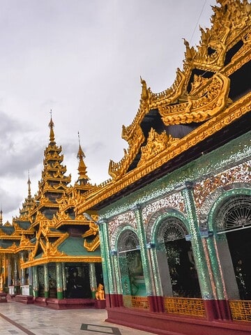 Golden Shwedagon Pagoda with ornate buildings and visitors under a cloudy sky in Yangon, Myanmar.