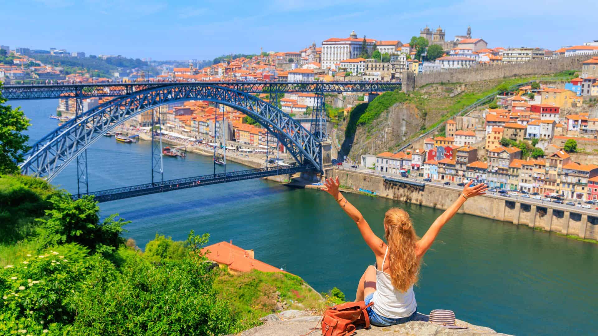 Woman with raised arms overlooks the Dom Lu&iacute;s I Bridge and colorful buildings by the river in Porto, Portugal.