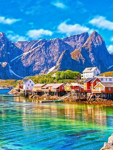 Colorful houses on a calm fjord with towering mountains in the background under a bright blue sky.