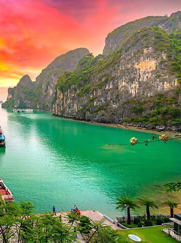 Boats float on turquoise water surrounded by limestone cliffs under a vibrant, colorful sunset sky—an idyllic scene reminiscent of Countries That Will Be Affordable in 2026.