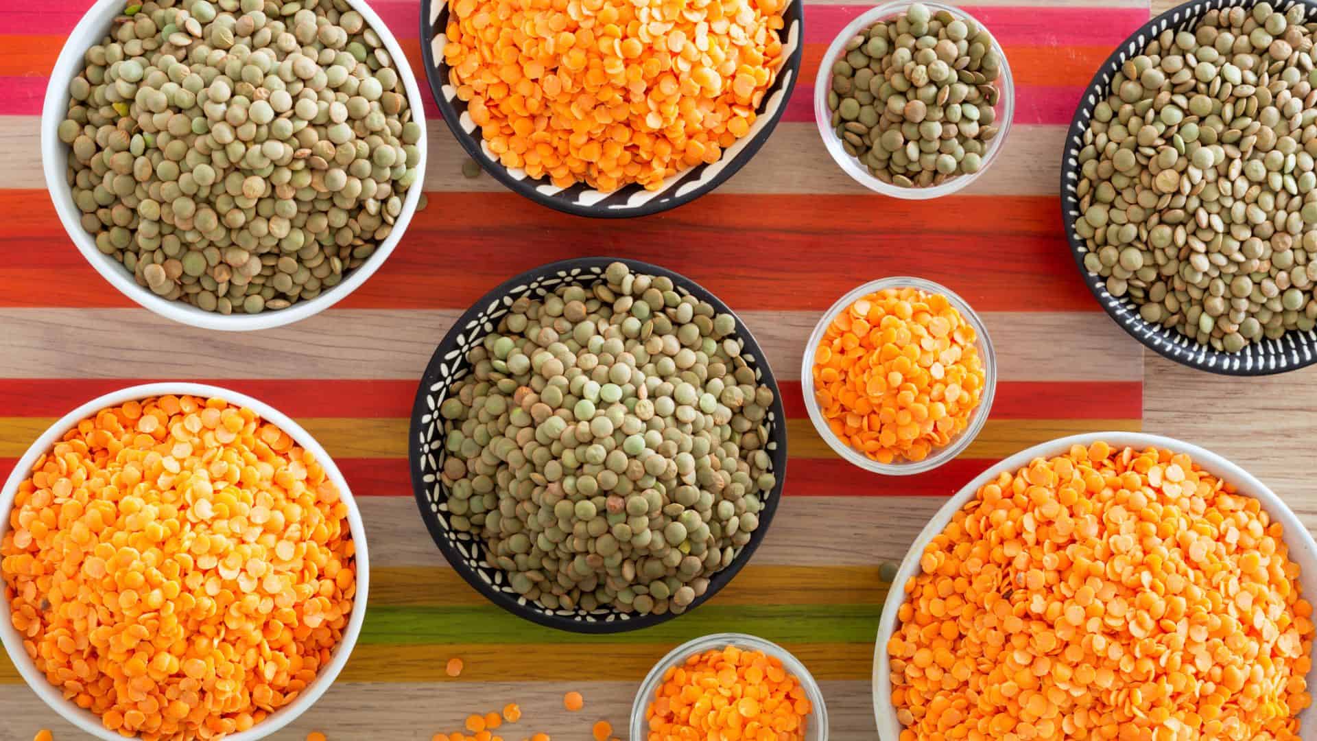 Bowls filled with green and orange lentils arranged on a colorful striped wooden surface.