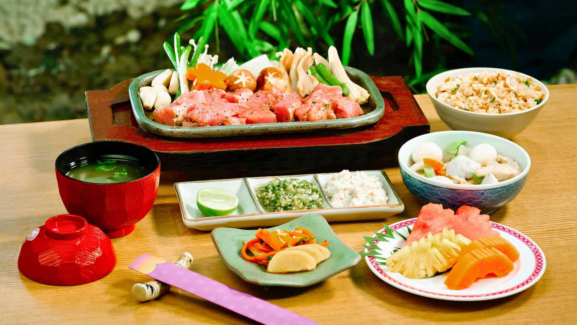 Japanese meal with grilled meat and vegetables, rice, soup, pickles, and assorted small side dishes on a table.