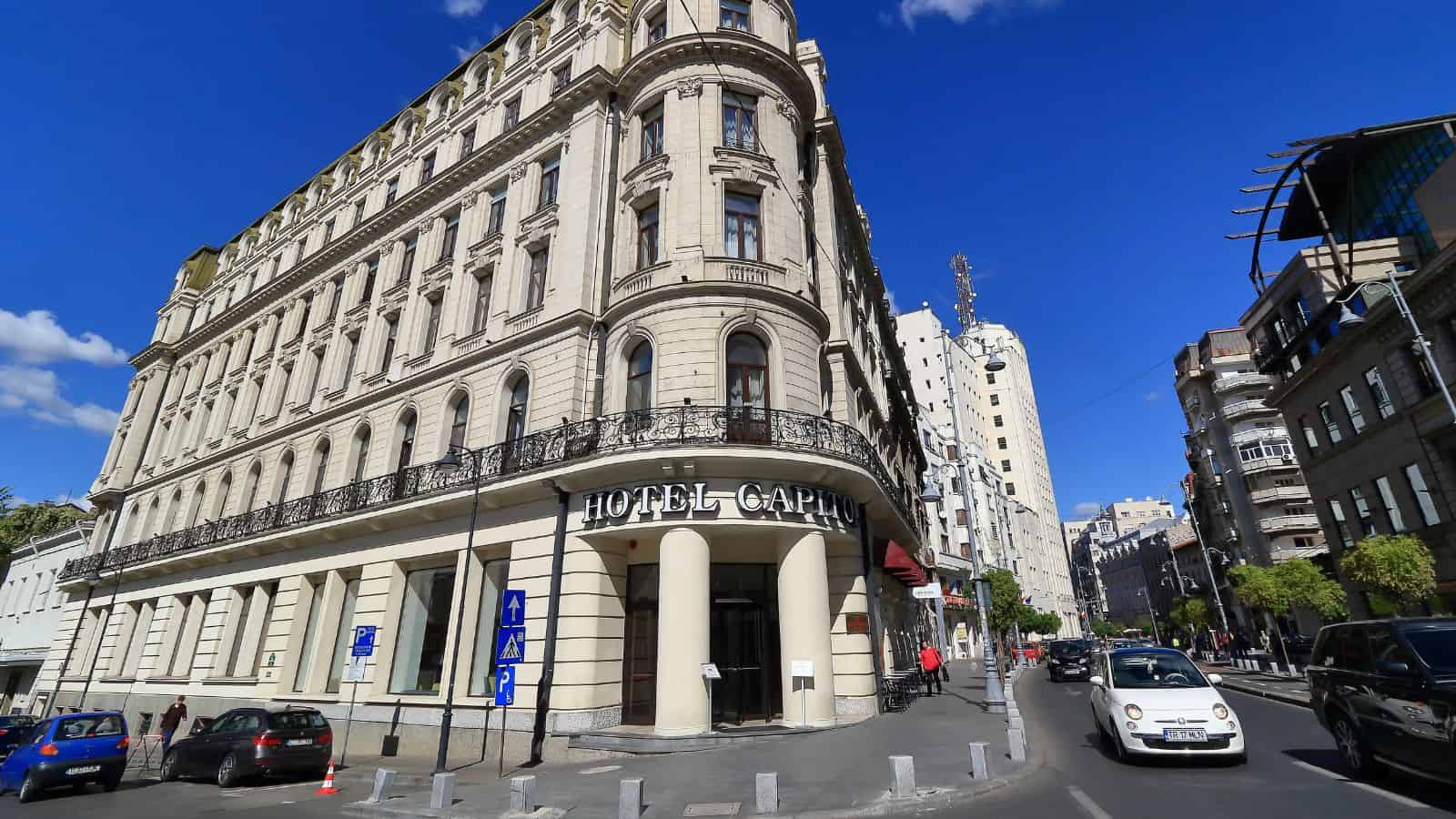 Corner view of Hotel Capitol, a grand historic building on a sunny city street with cars and blue sky&mdash;ideal for travelers over 35 seeking classic charm and expert hotel booking tips.