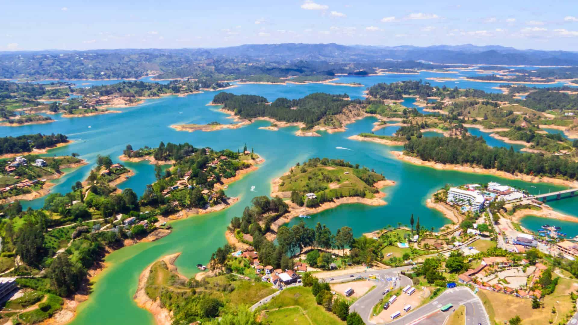 Aerial view of a lake with winding islands, greenery, and distant mountains under a blue sky.