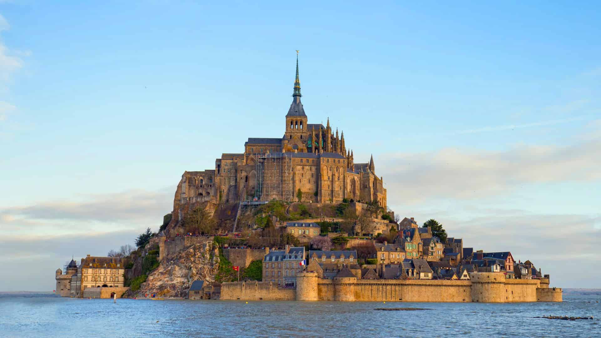 Mont Saint-Michel, a historic island abbey with stone buildings, rises above the sea under a blue sky.