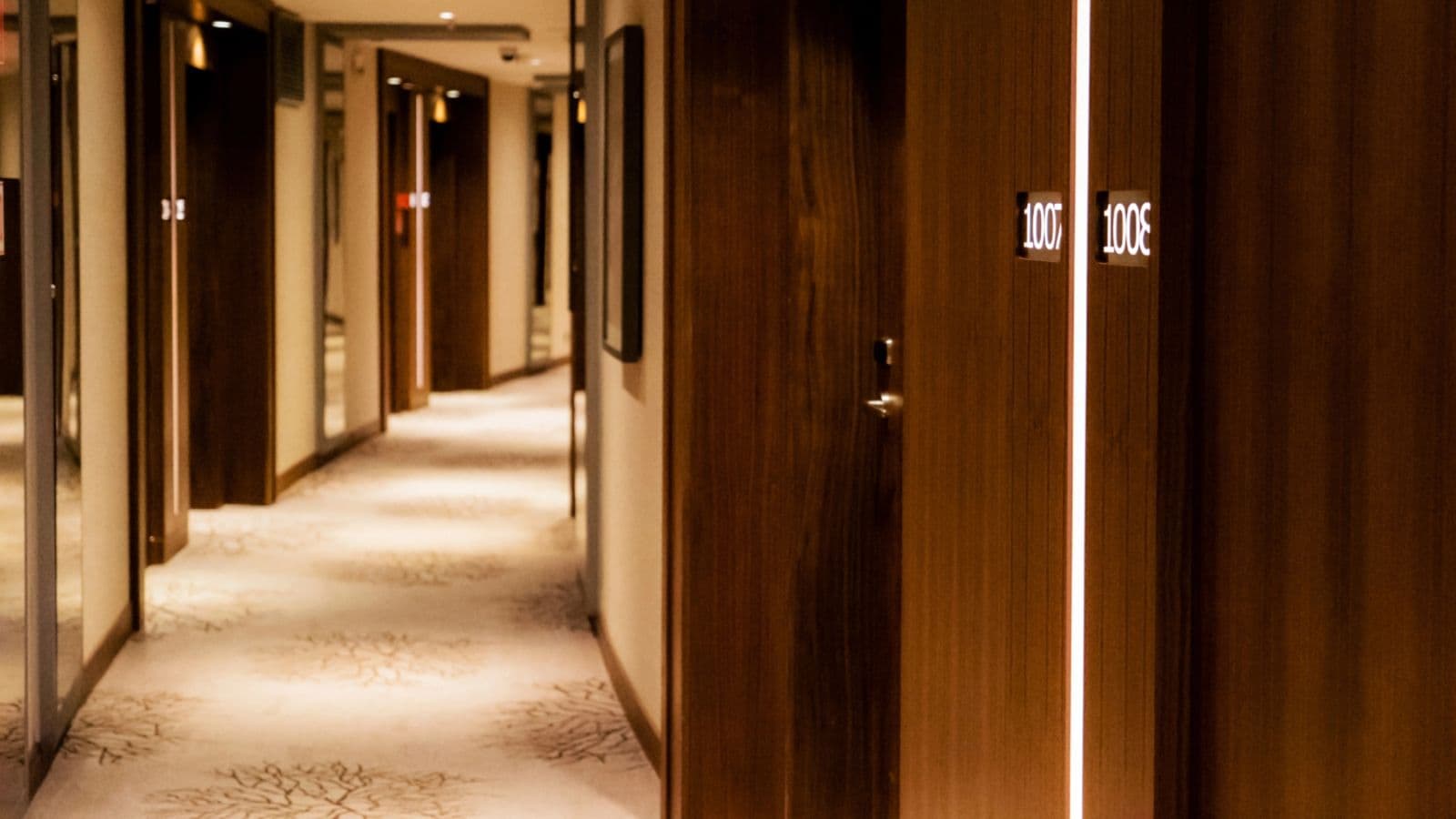 A modern hotel hallway with closed wooden doors and soft lighting along a carpeted floor&mdash;perfect for over 35 travelers seeking comfort after booking a hotel with expert travel tips.