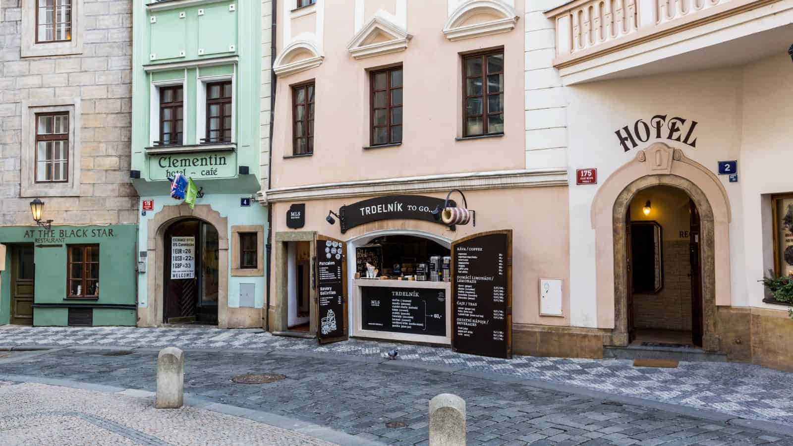 Colorful European street with caf&eacute;s, a hotel entrance perfect for those booking a hotel, and a takeaway bakery on a charming cobblestone sidewalk. Ideal for travelers over 35 exploring local flavors.