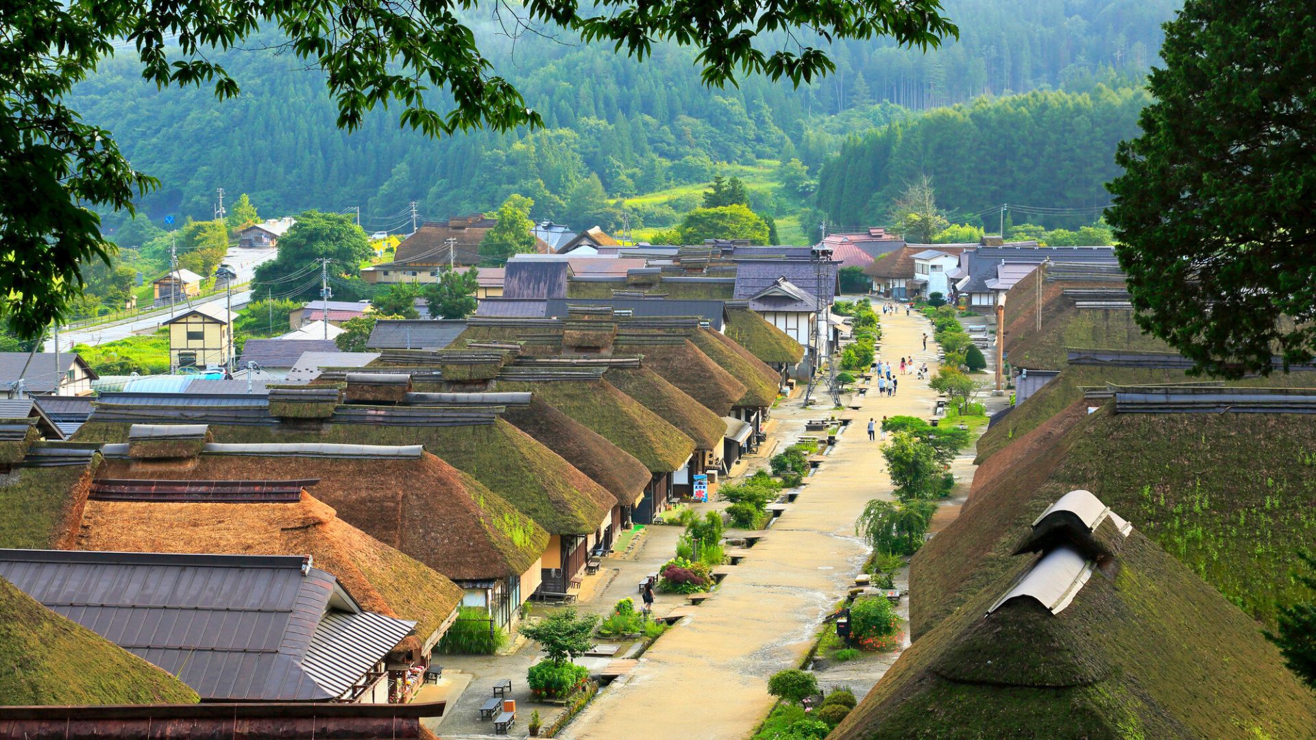 Traditional Japanese village with thatched roof houses surrounded by lush greenery and trees.