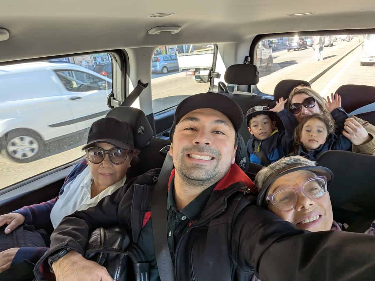 Six people of different ages smiling and posing for a selfie inside a car on a sunny day, capturing the joy of their 24 hours in Genoa, Italy.