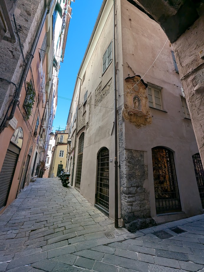 Narrow stone-paved alley flanked by tall, old buildings under a clear blue sky—discover this charming scene as you spend 24 hours in Genoa, Italy.